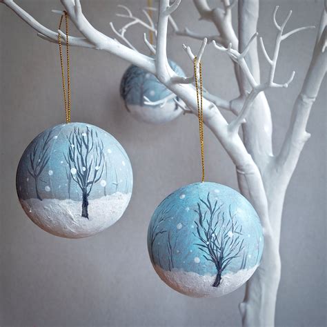 Three Ornaments Hanging From A White Tree With Snow On The Ground And