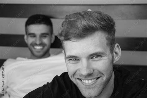Gay Lovers Sitting In Bed With One Close To Camera And The Other Looking On Both Are Smiling