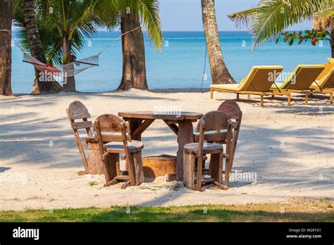 Tropical Sand Beach With Wooden Table And Chairs Chaise Lounges