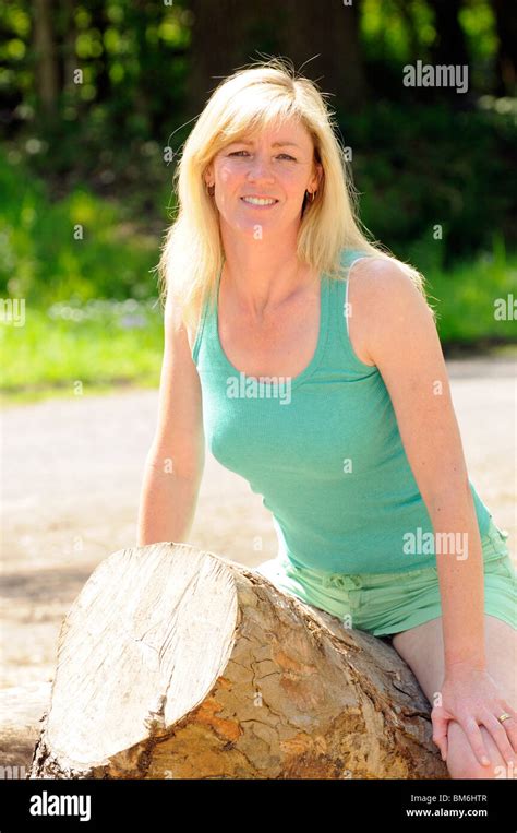 Portrait Of A Mid Forties Blonde Woman Outdoors Sitting On A Felled