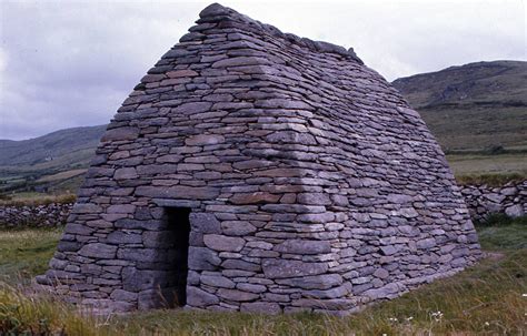 An Old Stone Building In The Middle Of A Field With Mountains In The