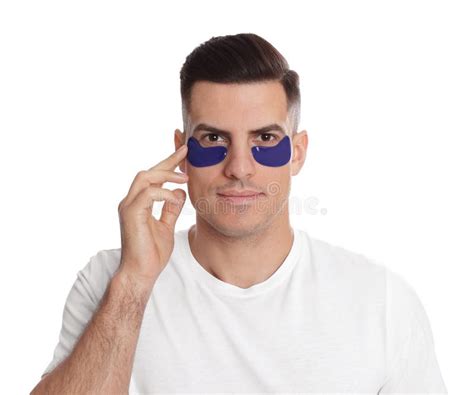 Man Applying Blue Under Eye Patch On White Background Stock Photo