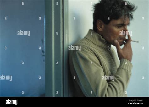 Mature Man Smoking Cigarette Leaning Against Wall Next To Open Doorway