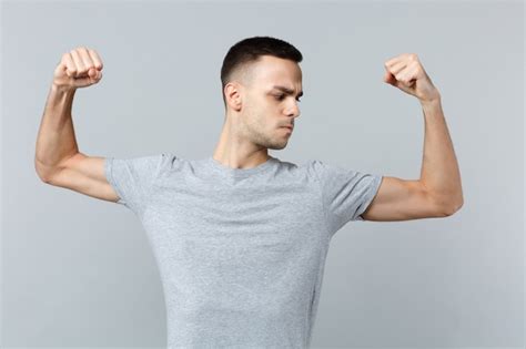 Retrato de um jovem forte em roupas casuais espalhando as mãos mostrando olhando nos bíceps e