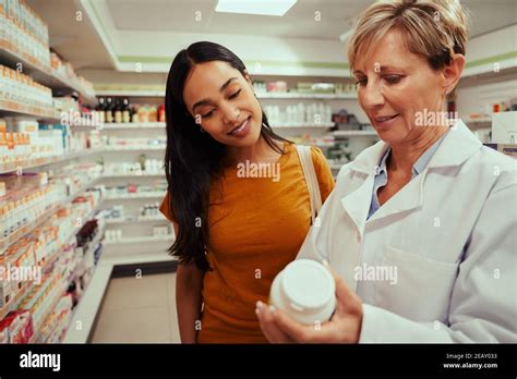 Senior Pharmacy Woman Helping Female Customer Find Bottle Of Medicine