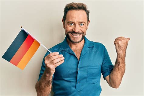 Middle Age Man Holding Germany Flag Pointing Thumb Up To The Side