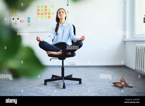 Serene Young Woman Meditating While Sitting On Office Chair Stock Photo