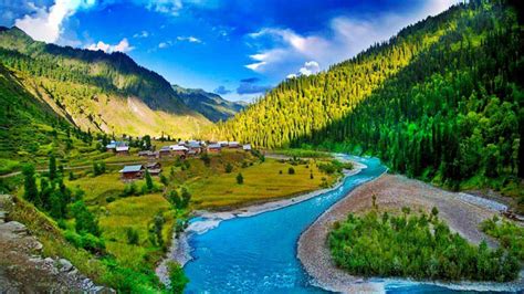 A River Flowing Through A Lush Green Valley Under A Blue Sky With