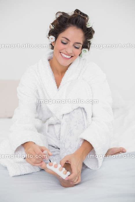Happy Natural Brunette Applying Nail Polish To Her Toenails In Bedroomの