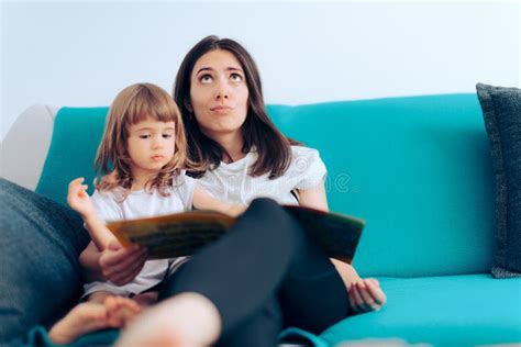 Tired Mother Reading To Her Daughter A Story At Home Stock Photo