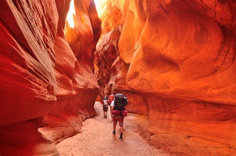 Two People Are Hiking Through The Narrow Canyons In The Desert With Red Walls