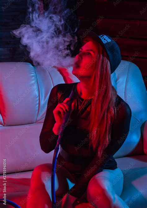 Sexy Redhead Woman In Black Bodysuit Sitting On A Sofa And Smokes