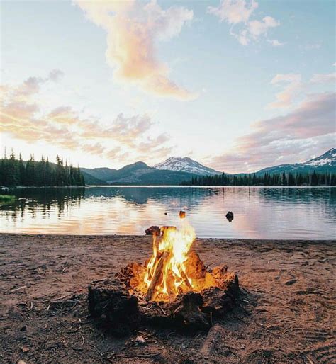 A Campfire On The Shore Of A Lake With Mountains In The Background