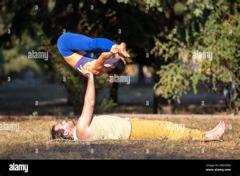 Young Couple Doing Acroyoga Exercises In Park Man Holding Woman On