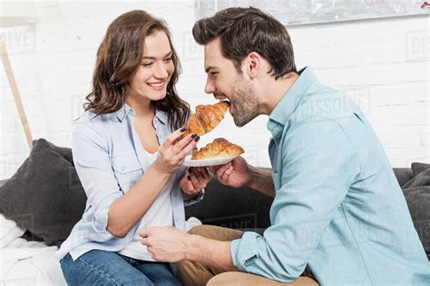 Beautiful Smiling Woman Feeding Man With Croissant During Breakfast At