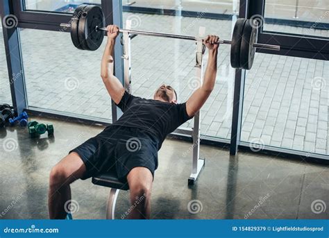 Handsome Sportive Man Lifting Barbell With Weights While Lying On Bench