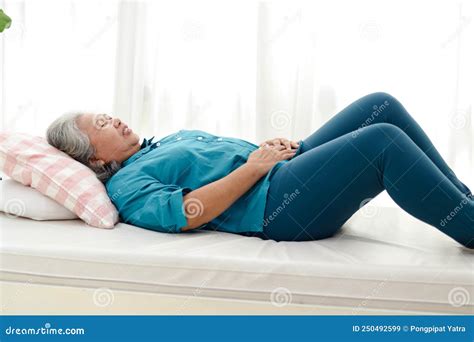 An Elderly Asian Woman Lies In Bed With Acute Abdominal Pain At Home