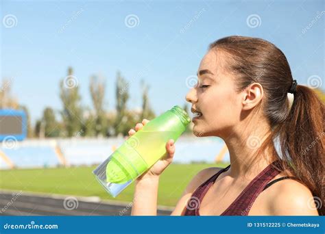 Young Sporty Woman Drinking Water From Bottle At Stadium On Sunny Day