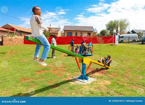 African Kids Playing On Seesaw And Other Park Equipment At Local Public