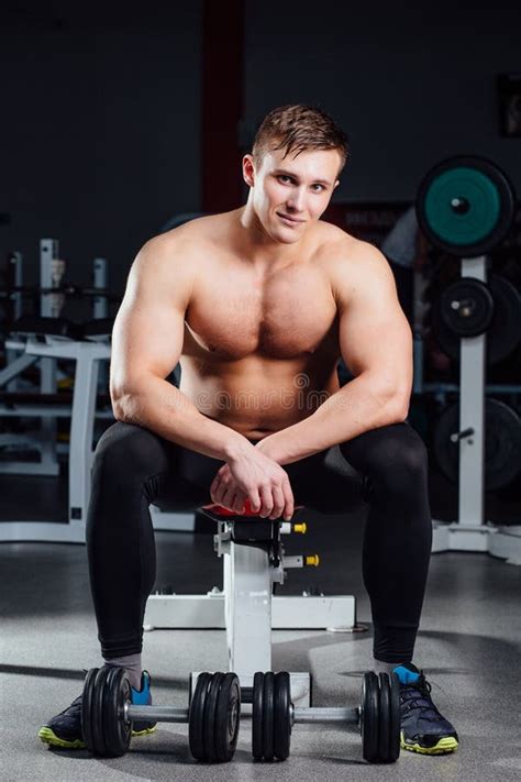 professional bodybuilder sitting on the bench resting between exercises with dumbbells at gym