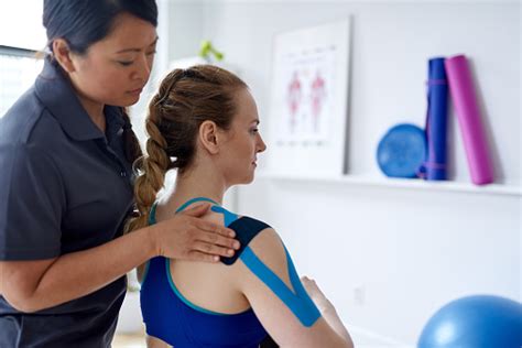chinese woman massage therapist applying kinesio tape to the shoulders and neck of an attractive