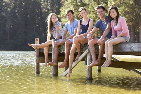 Group Of Young Friends Sitting On Wooden Jetty Looking Out Over Lake