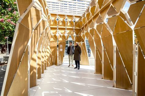 Two People Walking Down A Walkway With Wooden Structures