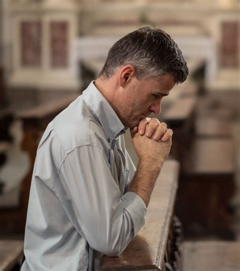 Religious Man Kneeling At The Pew In The Church And Praying With Hands