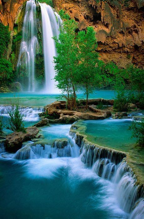 The Waterfall Is Surrounded By Green Trees And Blue Water In This
