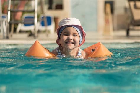 Happy Baby Girl Swims In Swimming Pool In Orange Armbands Vacation