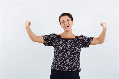 free photo mature woman in floral blouse and black skirt showing winner gesture and looking