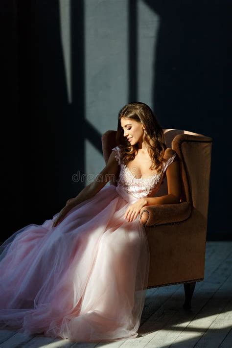 Delicate Beautiful Girl In A Pink Dress Smiles And Sits In A Chair In