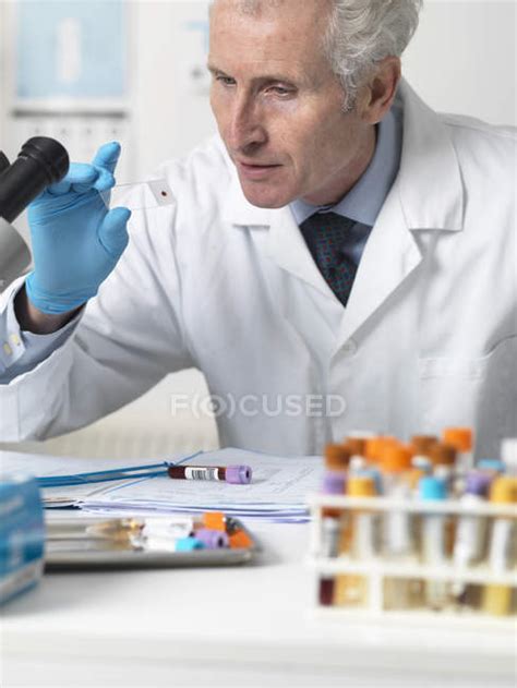 Doctor Looking At Patients Blood Slide Under Microscope With Other