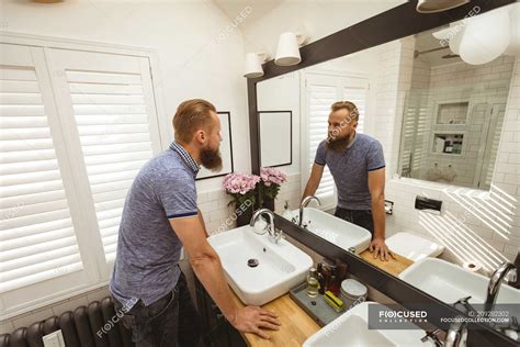 Hombre de pie frente al espejo revisándose en el baño Cabello rubio