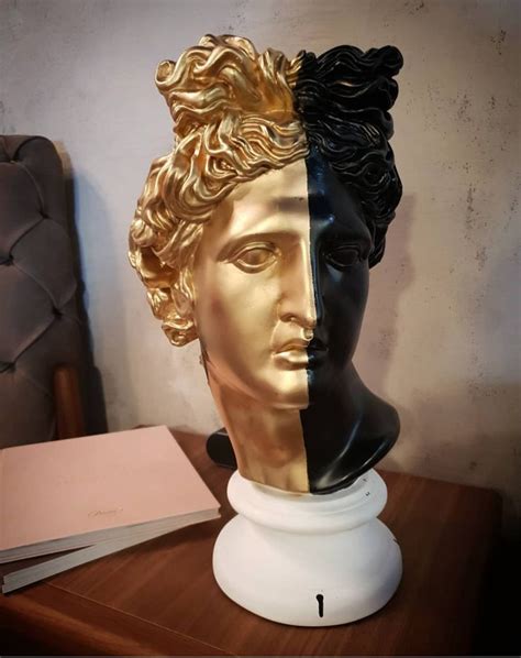 A Gold And Black Bust Sitting On Top Of A Wooden Table Next To A Book