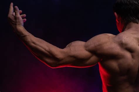 Мускулистый мужчина показывает мышцы изолированные на черном фоне с цветным дымом Премиум Фото
