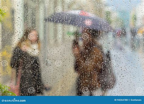Abstract Blurred Silhouettes Of People With Umbrellas On Rainy Day In