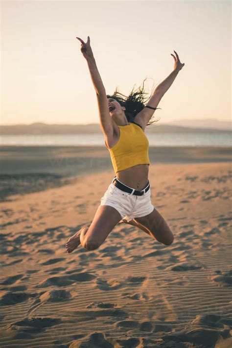 Happy Teenage Girl Jumping In The Air On The Beach At Sunset Stock Photo