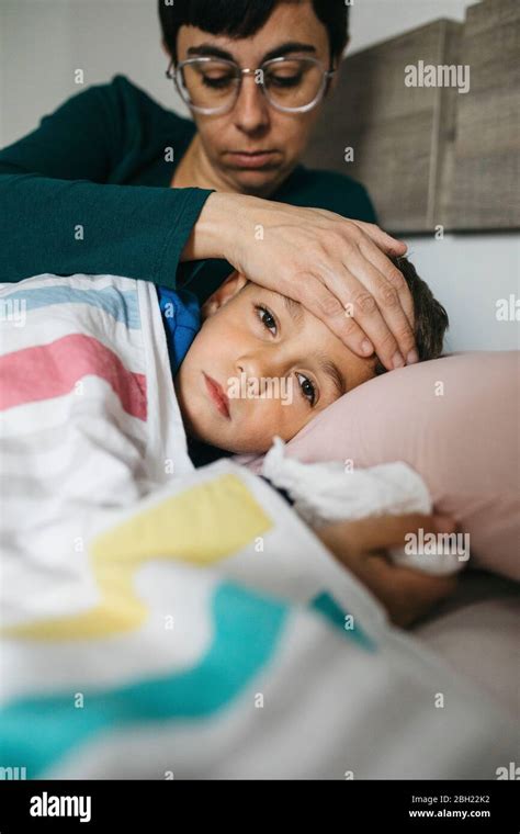 Retrato De Un Niño Enfermo Acostado En La Cama Mientras Su Madre Toca La Frente Fotografía De