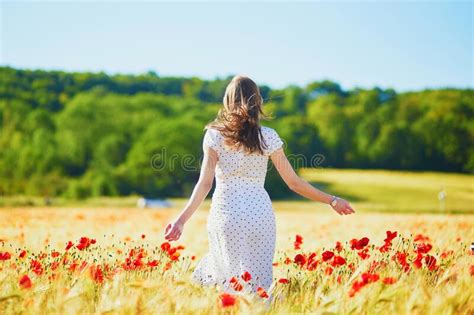 Beautiful Young Woman In White Dress Walking In Poppy Field On A Summer