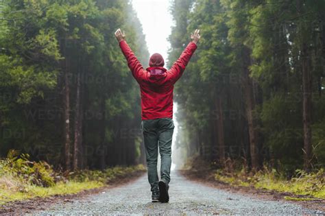Young Man With Hands Raised Walking On Forest Road Stock Photo
