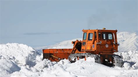 Orange Bulldozer Clearing Deep Snow Off Mountain Road In
