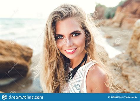 Closeup Portrait Of Pretty Blonde Girl In Sunlight Posing On Rocky Beach She Wears Black Bikini