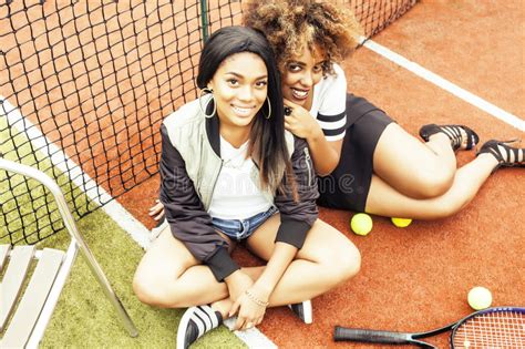 Молодые милые подруги вися на теннисном корте фасонируют стильный