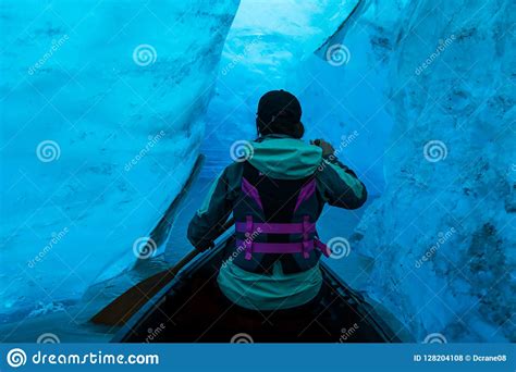 Woman Paddling Canoe Into The Ice Cave Of A Glacier In Alaska Stock