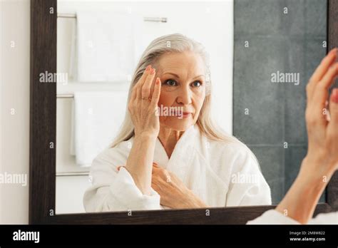 Aged Woman Looking At A Mirror And Touching Her Face Female With Grey