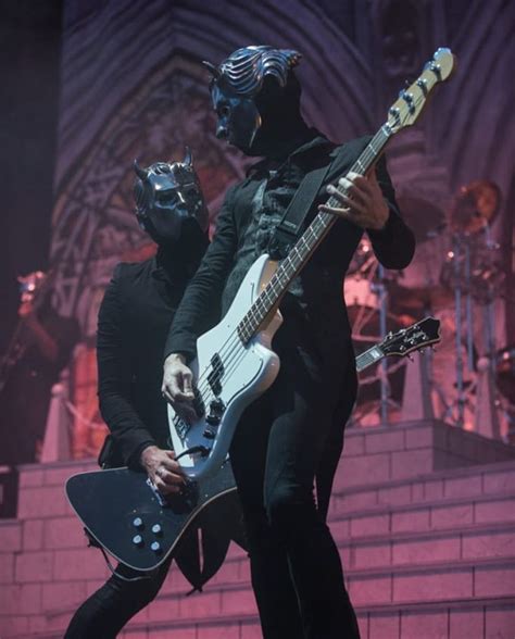 Two Men In Black Costumes Playing Guitars And Wearing Masks On Their
