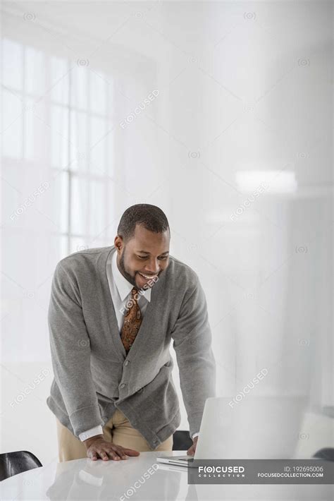 Mid Adult Man Leaning Over Table And Using Laptop In Office — Business