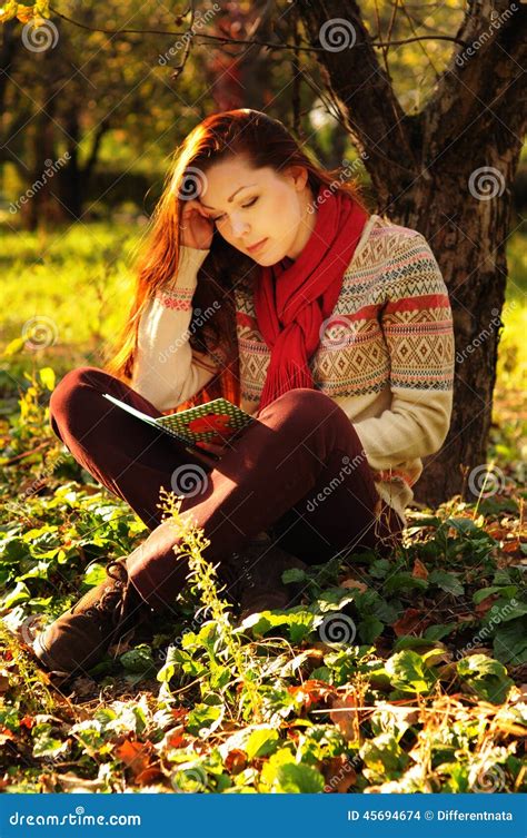 Young Woman With Long Red Hair Reading Under The Tree Stock Photo
