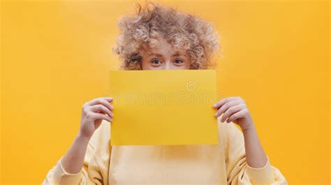 Girl Holding A Yellow Sheet Of Paper Covering Half Of Her Face
